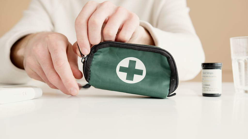 Close-up image of hands holding a first aid pouch on a table, with medical test strips nearby.